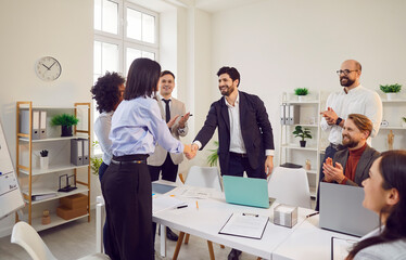 Happy coworkers shaking hands during a work meeting in the modern office, surrounded by colleagues....
