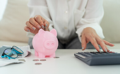 Person saving money inserting coin into pink piggy bank while calculating budget, personal finance, budgeting and financial planning at home with calculator, financial goal management, cost control