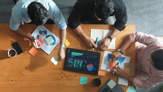 Top aerial view of diverse team writing colorful sticky notes to brainstorm marketing idea while looking at financial chart. Multicultural smart business people taking a note about plan. Convocation.
