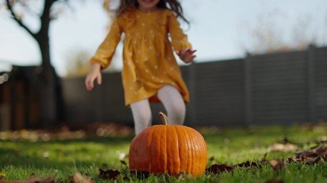 Happy little girl playing with pumpkin in the backyard