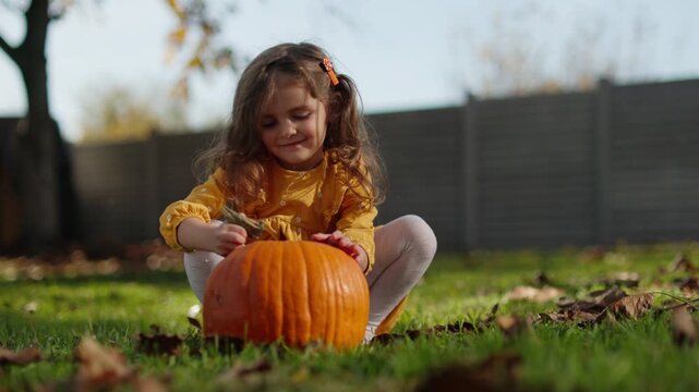 Happy little girl playing with pumpkin in autumn backyard