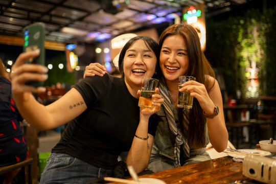 Happy asian friends taking selfie enjoying beer at bar