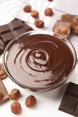 Melted chocolate and pieces with hazelnuts on white wooden table, closeup