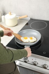 Woman taking fried eggs with slotted spatula in kitchen, closeup