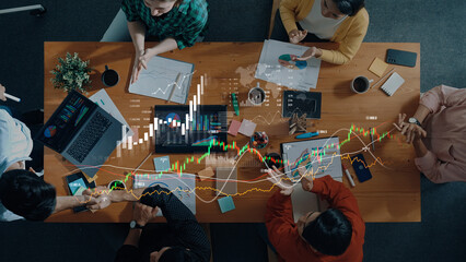 Aerial view of a collaborative business meeting where professionals analyze data on laptops, papers, and graphs, emphasizing teamwork and strategic planning in a modern workspace. Scalp