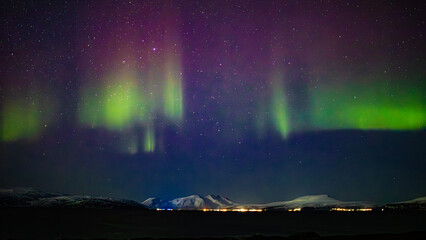 Green and red Northern Lights stretch across the Arctic night sky full of stars, creating a...