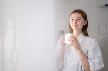 A young woman and a new morning with warm coffee, standing in the morning