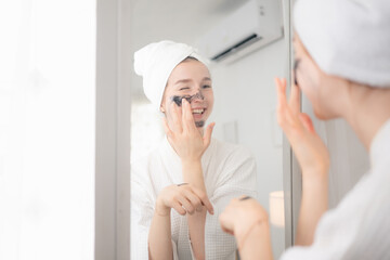 A young woman stands in front of a mirror and performs a natural facial skin care