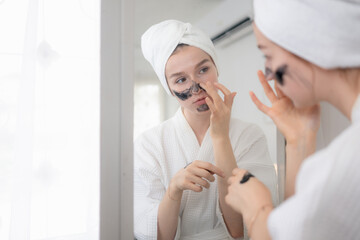 A young woman stands in front of a mirror and performs a natural facial skin care