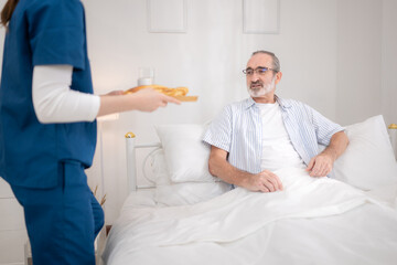 Obraz premium A female nurse assists an elderly patient in bed with food and medication before meals