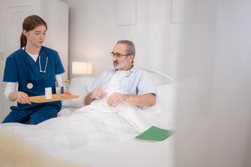 A female nurse assists an elderly patient in bed with food and medication