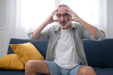 Fototapeta premium An elderly man sitting on a sofa with a headache, exhibiting symptoms of stress