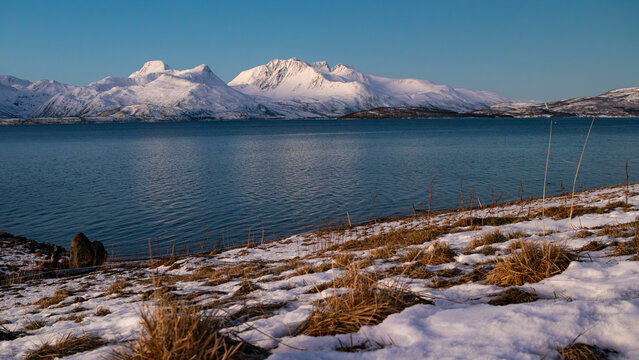 Fjord of tromso norway with Snow-covered mountains reflecting over calm blue lake in early spring