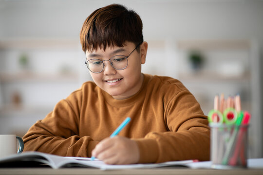 A happy asian school boy is sitting at a table, focused on his homework.