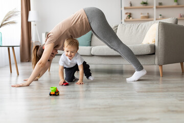 A mother engages in playful activity with her young child on the living room floor. They are...