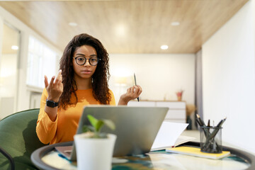 A young woman in an orange shirt sits at a table in a stylish workspace. She appears focused and...