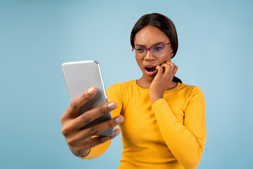 A woman with glasses looks surprised and anxious while checking her smartphone. She has a concerned...