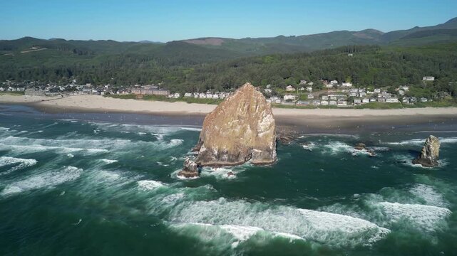 Cinematic aerial drone footage circling Haystack Rock at Cannon Beach, Oregon, showcasing the north side of the landmark with ocean waves, beach, and coastal town view
