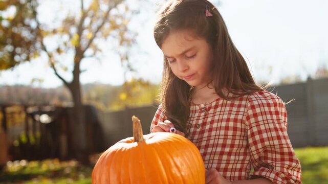 Little girl drawing a scary face on a pumpkin for halloween