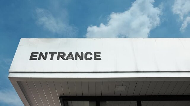 Entrance word sign clearly displayed near the main doorway of a commercial or public building facade beneath a clear blue sky, signifying the primary point of access.
