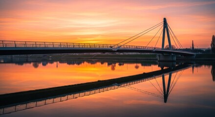 Obraz premium Sunrise over a calm river, with a modern pedestrian bridge reflected perfectly