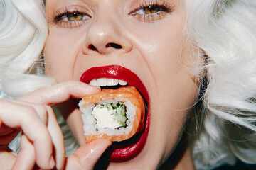 Close-up of a fashionable woman with platinum blonde hair and red lips enjoying sushi roll in a...