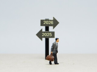 Mini toy of action figure at outdoor with blurred background. Miniature photography concept design. Minifigure of people character at street with 2025 2026 traffic sign. New year resolution.