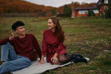Candid portrait of a young couple sharing a genuine conversation while sitting on a blanket in a rustic meadow, captured with natural light and authentic, relaxed expressions conveying real