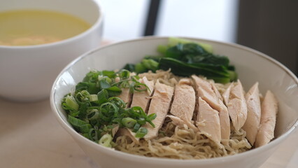 Authentic free-range chicken noodles in a white bowl with mustard greens and chopped scallions. Mie ayam kampung.