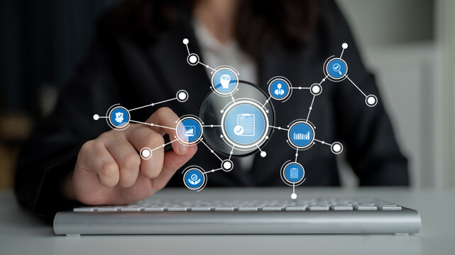 A businesswoman in a suit uses a magnifying glass over a keyboard, interacting with a digital network of icons that symbolize data analysis and information research. Tessel