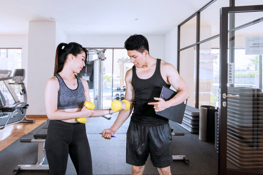 Female Client Consulting with Her Personal Trainer While Holding Dumbbells in a Modern Gym