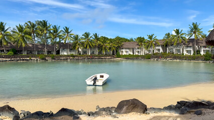Small white boat moored in a calm, turquoise lagoon in front of a row of palm-fringed tropical resort bungalows