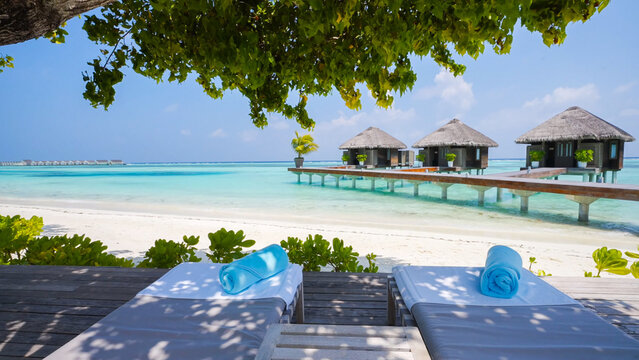 Tropical Maldivian overwater bungalows and a secluded white sand beach, viewed from a private shaded wooden deck with lounge chairs
