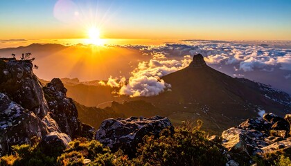 A breathtaking sunrise illuminates a craggy mountaintop, highlighting the distant, mist-shrouded peaks. The sky is ablaze with golden hues