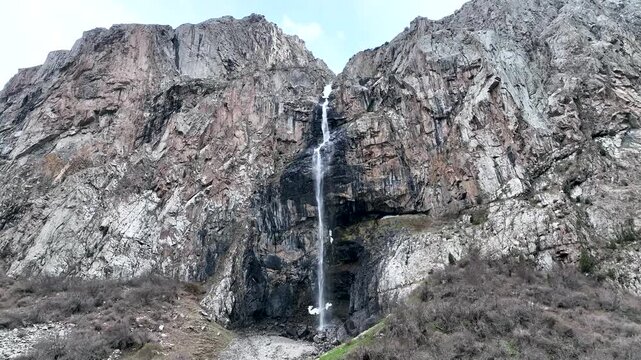 A spectacular narrow waterfall dropping from a narrow cleft between two towering, steep mountain rock faces and cliffs