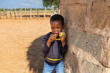 hungry african child in the village, eating biscuits next to the house in the yard