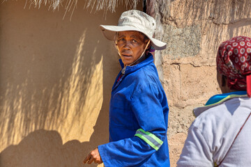 portrait old african woman village life, standing in front of the hut with thatched roof