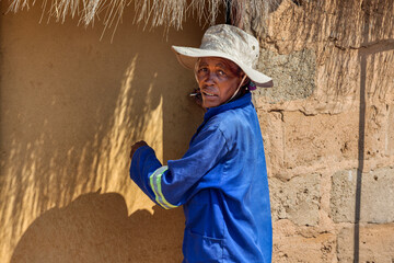 african village life, woman standing in the yard in front of the shack door with thatched roof