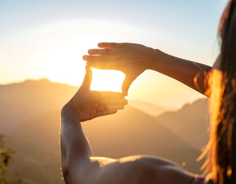 Person using hands to frame the sun over mountains