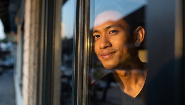 Young man looking out a window reflecting sunlight.
