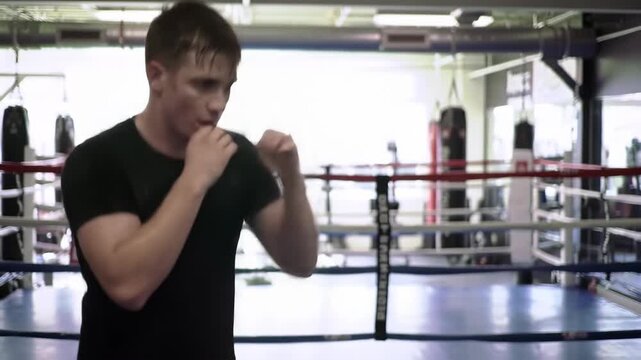 Boxer training inside boxing ring, shadowboxing with sweat, gym equipment visible in background. For fitness