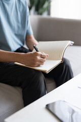 Asian Man Taking Notes on Finances, Budget, Household Expenses, and Tax Calculations in Notebook at Home.