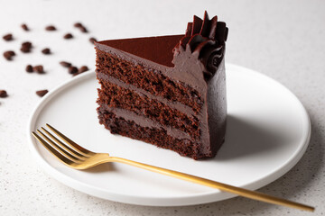 A slice of chocolate cake on a white plate with gold fork