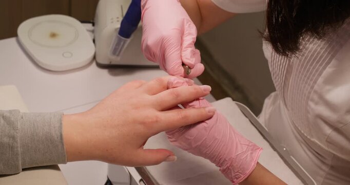 Nail manicure. Salon procedure. Beautician female master hands in protective gloves cutting cuticle skin on clients finger using forceps for beauty.