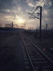 Obraz premium A tranquil railway scene at sunset, featuring silhouetted power lines and a dramatic, cloudy sky creating a peaceful and reflective atmosphere.