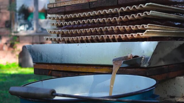Gorgeous golden brown and yellow apple juice being pressed from apple mush in a sunny garden with a juice press. Bokeh blurry background and shallow depth of field. Juice dripping between press slowly