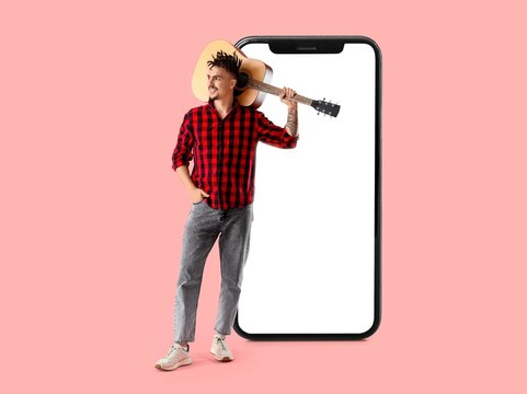 Big smartphone and cool young man with guitar on pink background