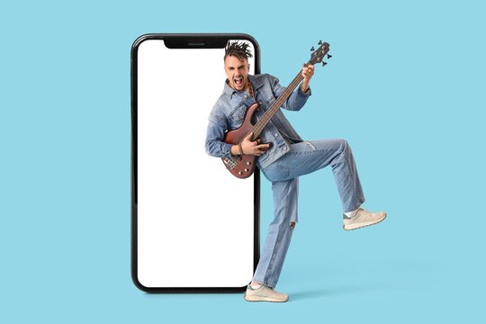 Big smartphone and cool young man playing guitar on blue background