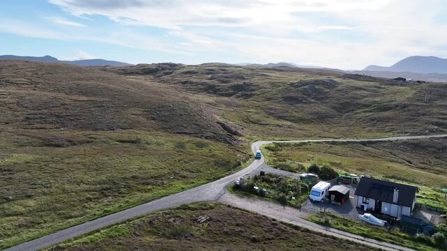 Drone captures a blue camper van departing a small cottage in the Scottish Highlands, heading onto the North Coast 500. A cinematic shot showing the freedom and solitude of remote Scottish travel.