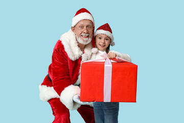 Santa Claus and cute little girl with gift box on blue background